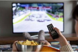 Persona sul divano con telecomando e patatine, guarda la TV