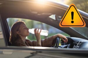 donna che beve acqua in auto e segnale pericolo